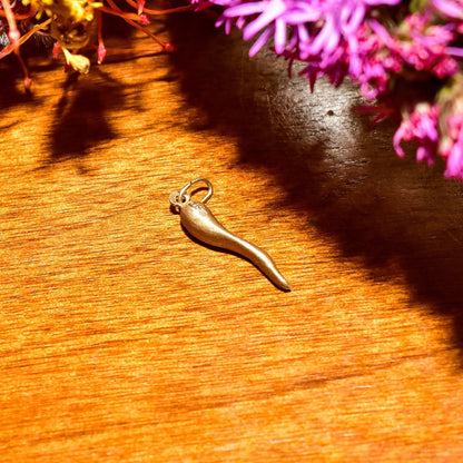 14K yellow gold Italian horn charm pendant on wooden surface with pink flowers in background