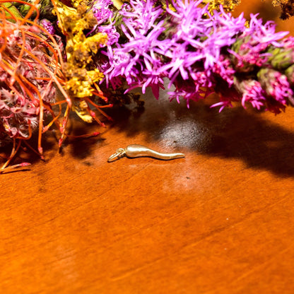 Pink and yellow flowers on a dark wooden table with a small gold Italian horn charm pendant in the foreground.