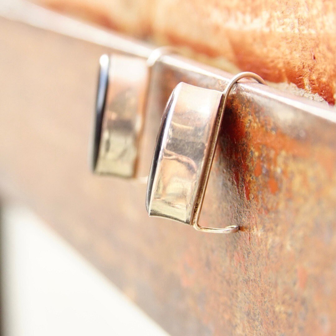 Close-up view of vintage sterling silver earrings with rectangular onyx stones, showing rusty patina on the metal surface. The earrings have simple geometric shapes and a latch-back closure mechanism.