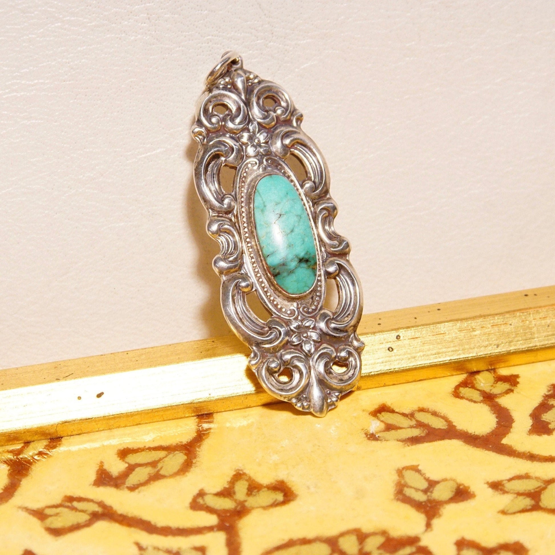 Vintage Towle sterling silver pendant with ornate embossed repousse designs, featuring a turquoise cabochon at the center. The pendant has an Art Nouveau style with intricate floral motifs and measures 2 3/4 inches in length.