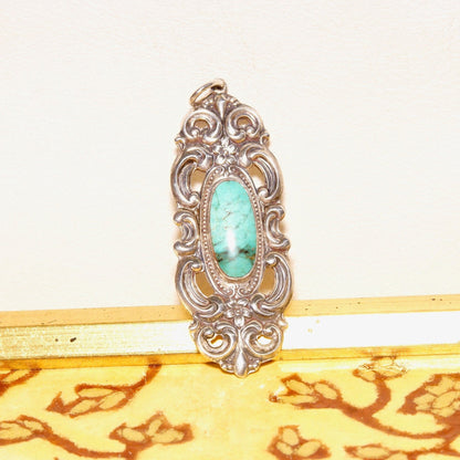 Vintage Towle sterling silver pendant with ornate embossed repousse designs, featuring a turquoise cabochon at the center. The pendant has an art nouveau style with intricate floral motifs and scrollwork, measuring 2 3/4 inches in length.