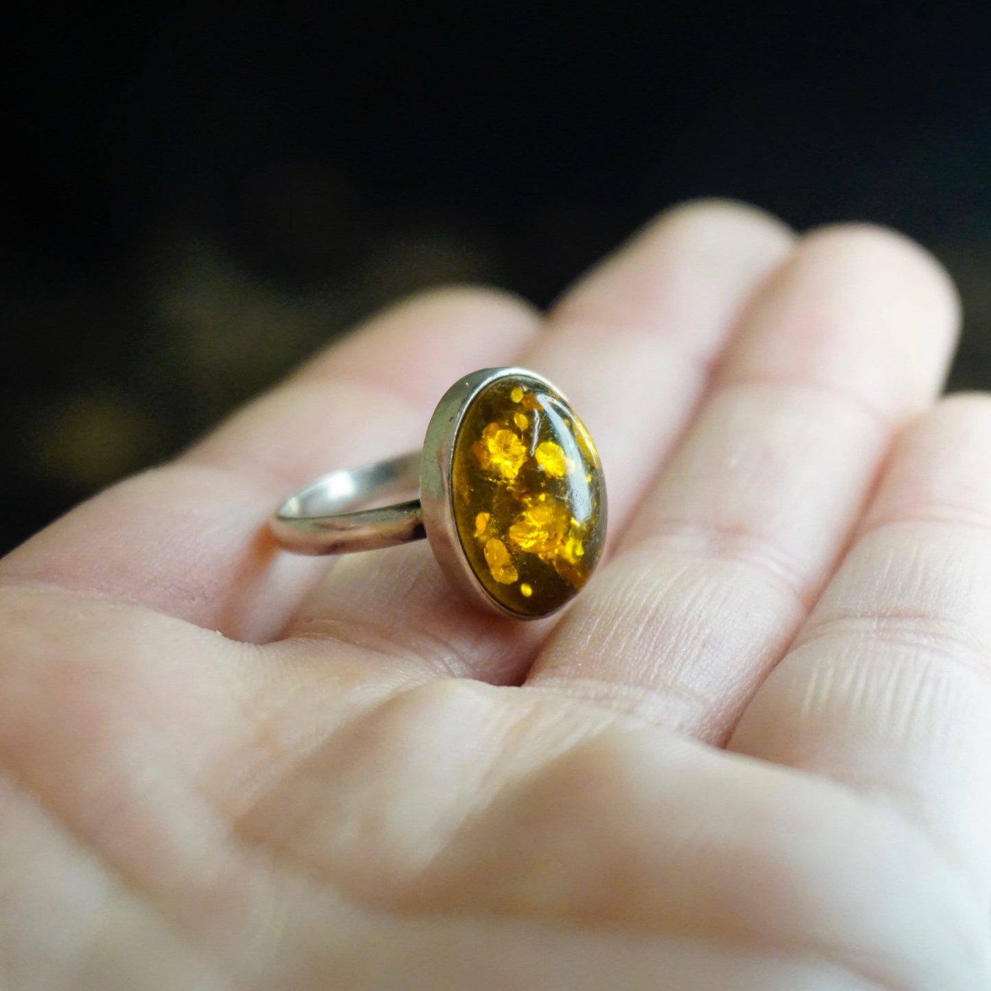 Vintage sterling silver ring with oval natural amber stone held in a hand, showcasing the amber's golden color and unique inclusions against the minimalist silver band.