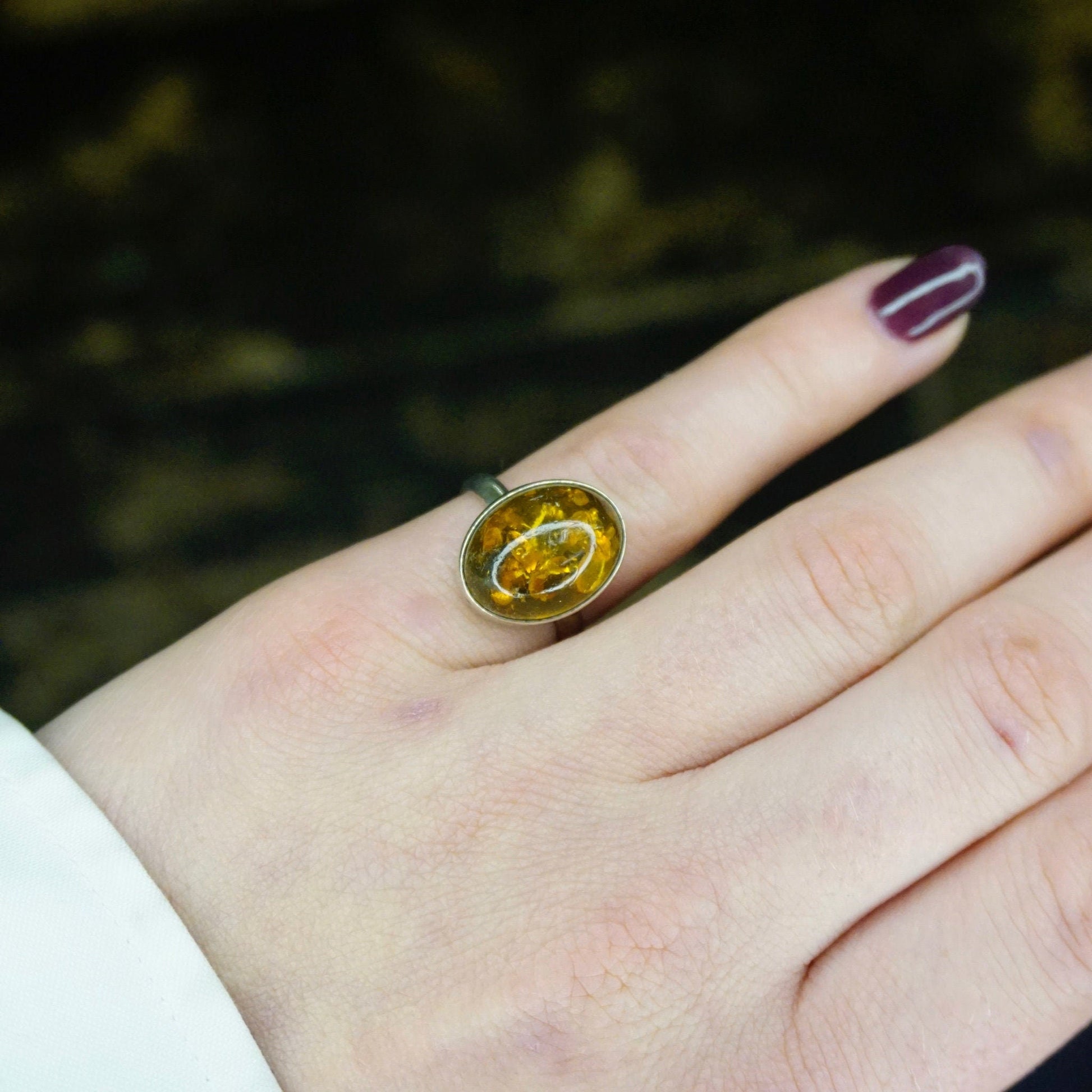 Vintage sterling silver ring with an oval-shaped amber stone displaying natural inclusions, set in a minimalist design, photographed on a hand against a dark background.