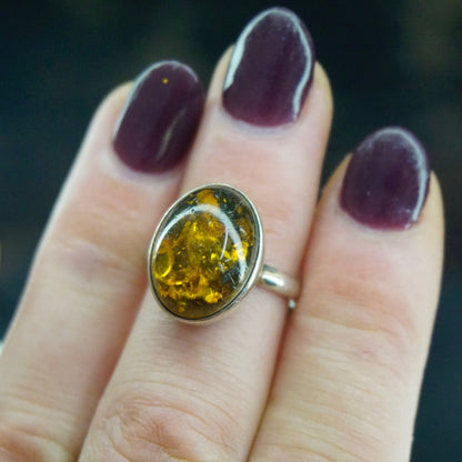 Vintage sterling silver ring with oval amber stone featuring natural inclusions, displayed on fingers with dark purple nail polish. Minimalist amber silver ring, 925 jewelry.