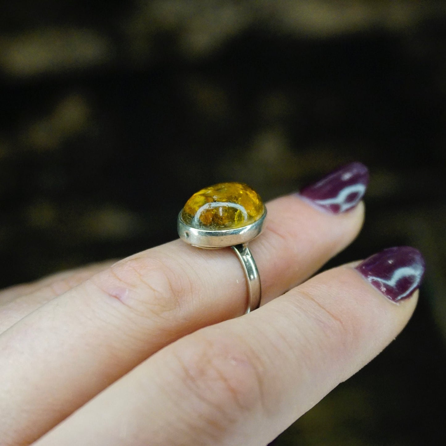 Vintage sterling silver amber ring on a finger, featuring an oval amber stone with natural inclusions set in a minimalist 925 silver band.