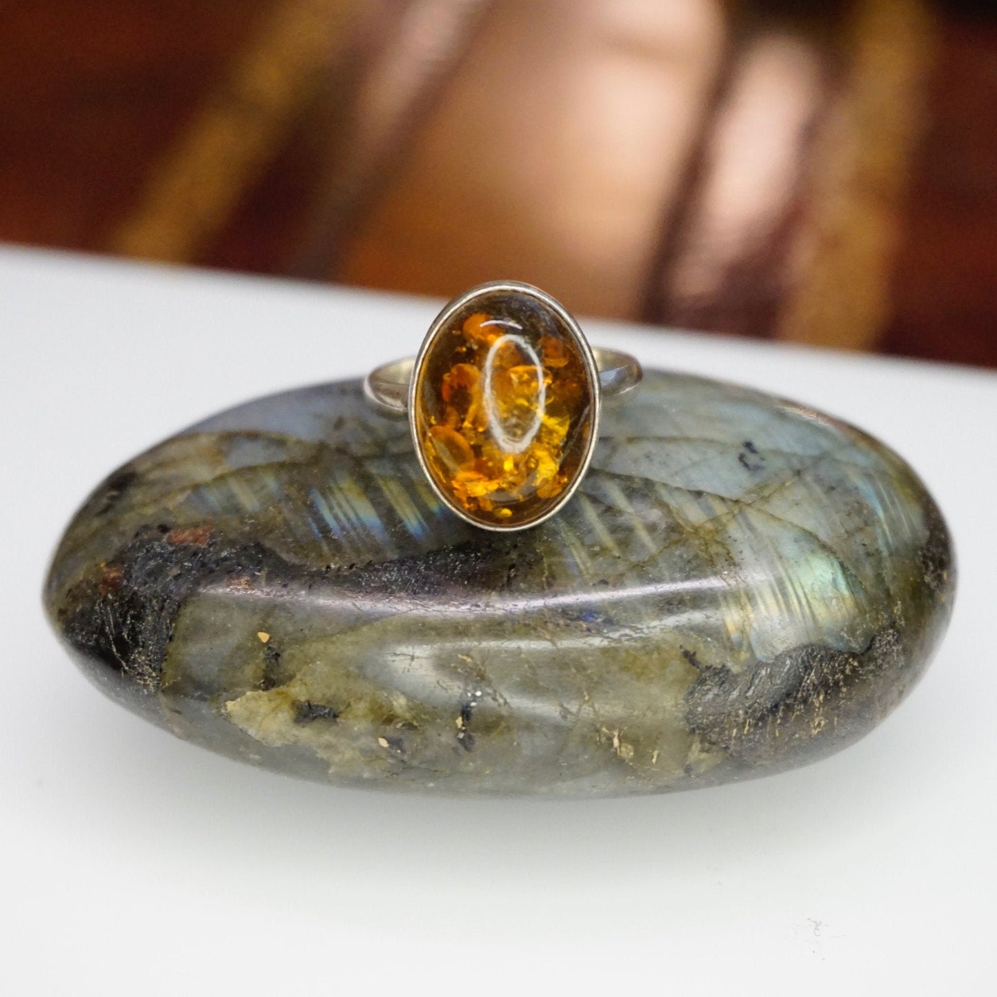 Vintage sterling silver ring with an oval amber stone displaying unique natural inclusions, set in a minimalist 925 silver setting on a textured gray background.