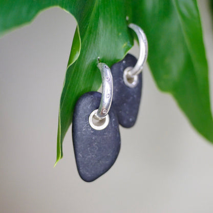 Vintage sterling silver hoop earrings with black stone charms hanging from green leaf, closeup view against neutral background.