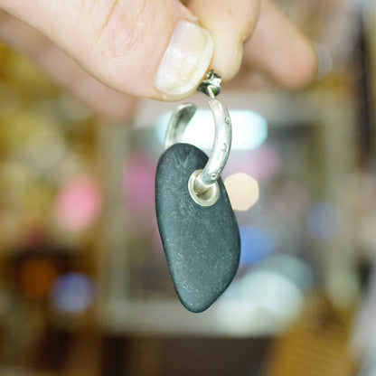 Vintage sterling silver hoop earrings with black stone charm held by hand against blurred background