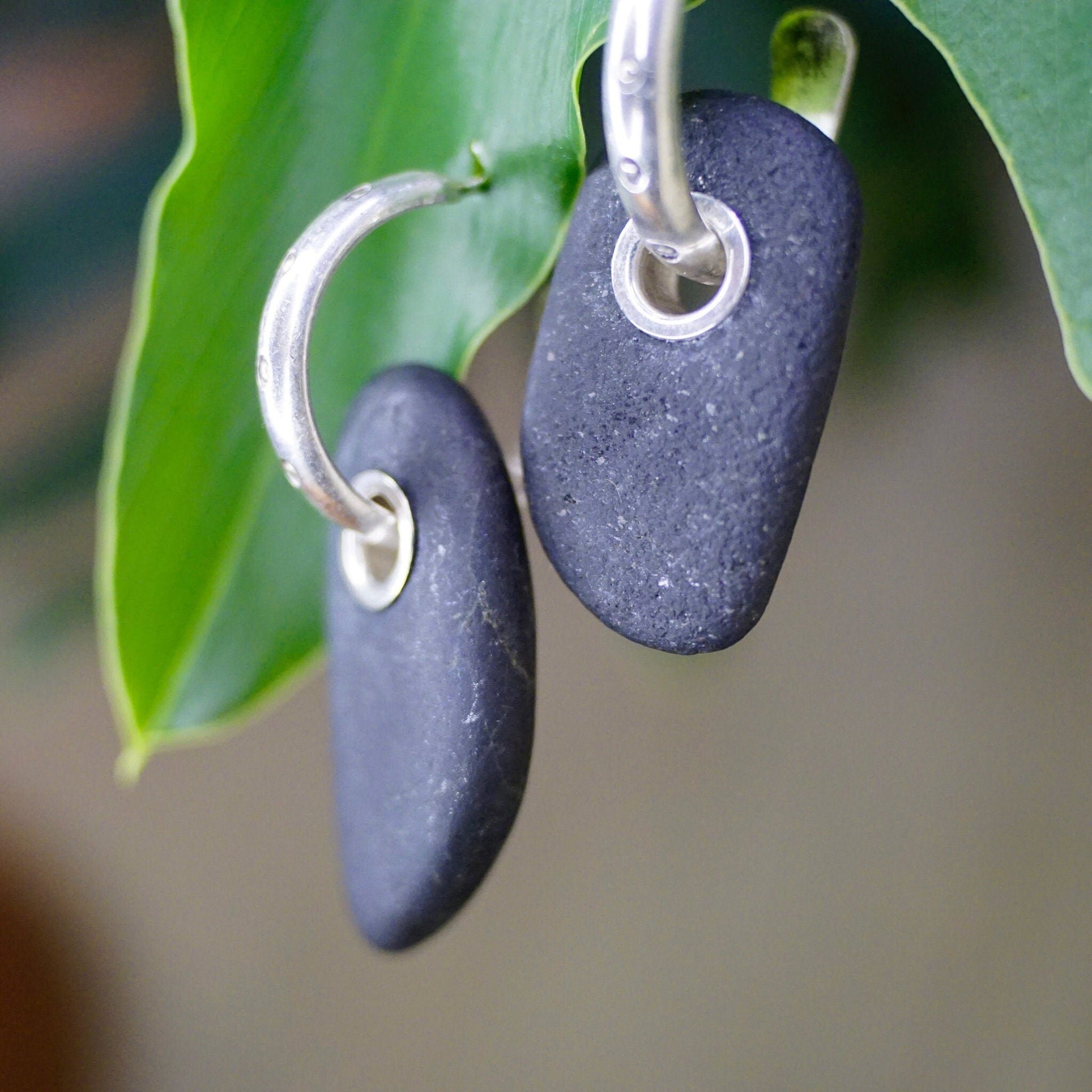 Vintage sterling silver hoop earrings with black stone charms on green leaf background, closeup view