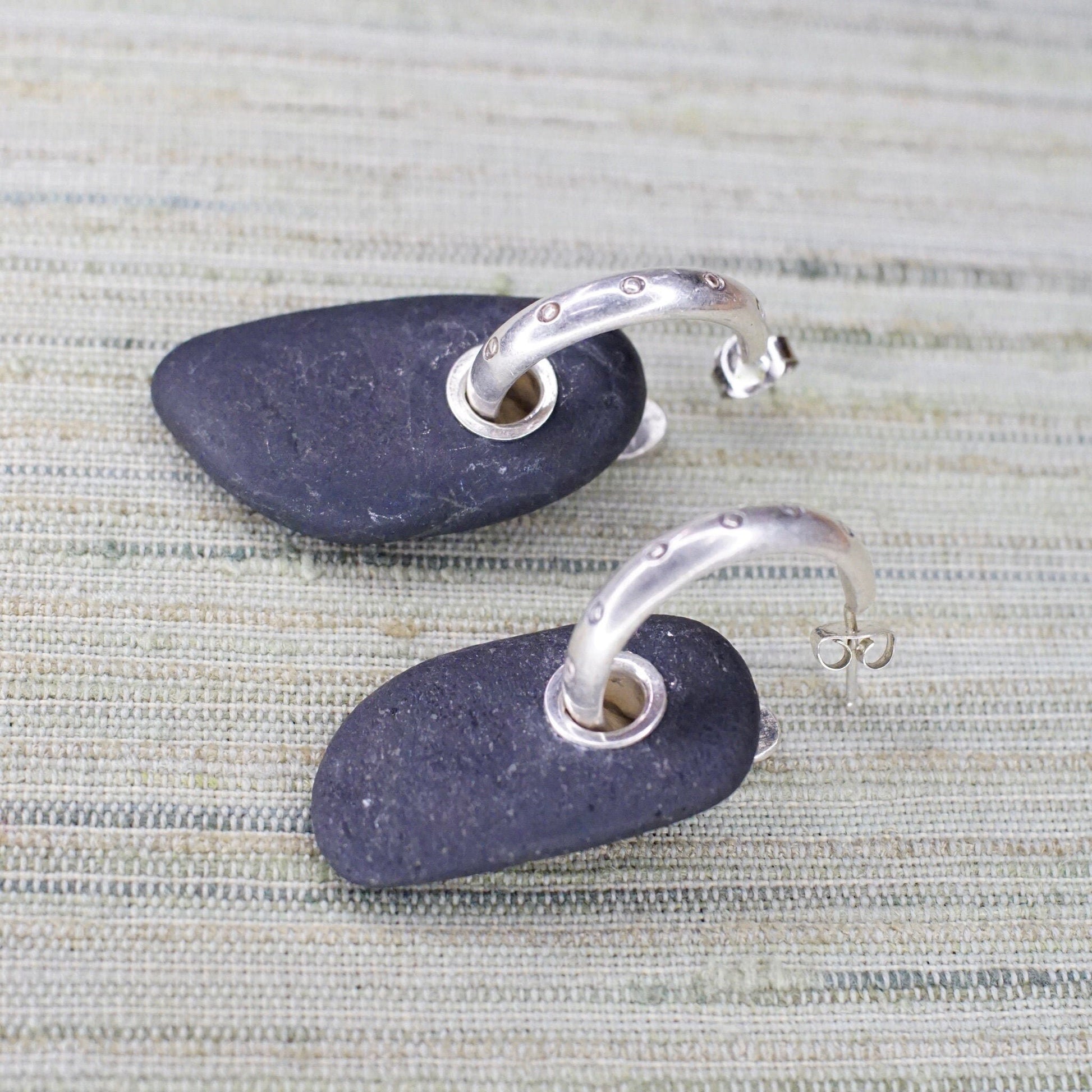 Vintage sterling silver hoop earrings with black stone charm threaded through the hoops, displayed on a neutral textured background.