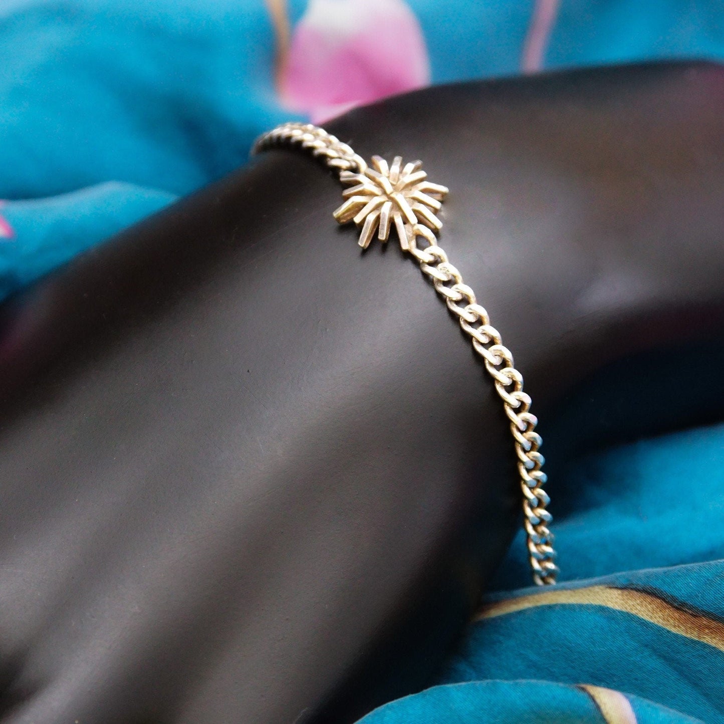 Vintage sterling silver curb link bracelet with starburst flower accent on dark skin, draped over blue fabric