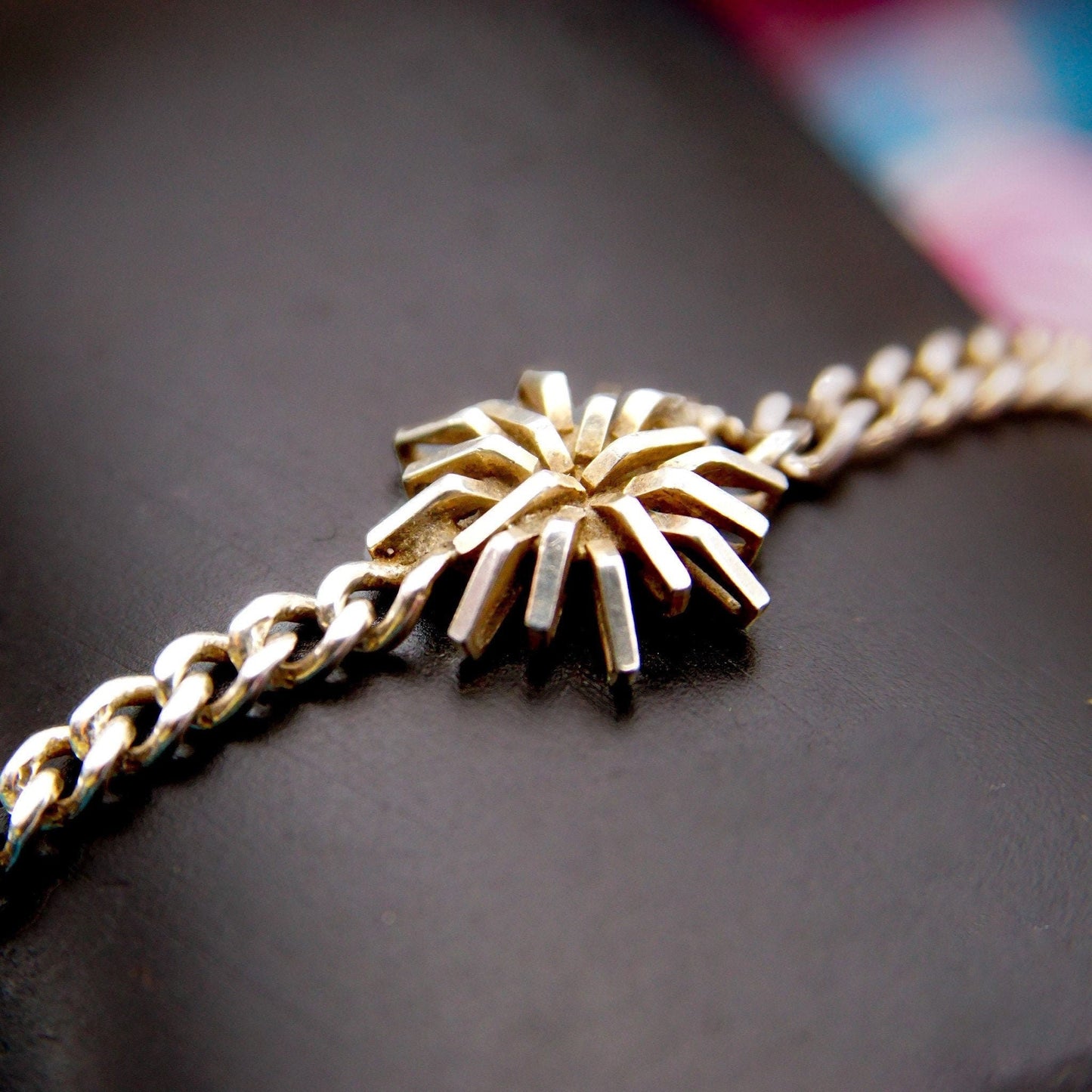 Vintage sterling silver curb link bracelet with geometric starburst flower accent on a dark background