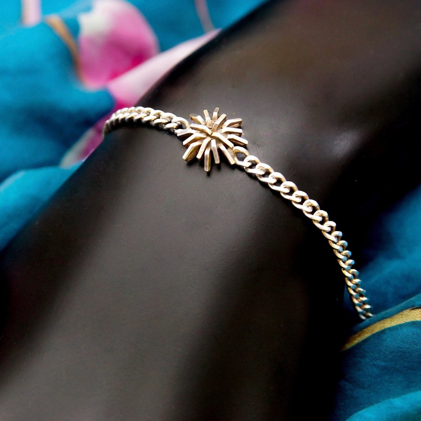 Vintage sterling silver curb link bracelet with starburst accent on a model's wrist, surrounded by blue fabric