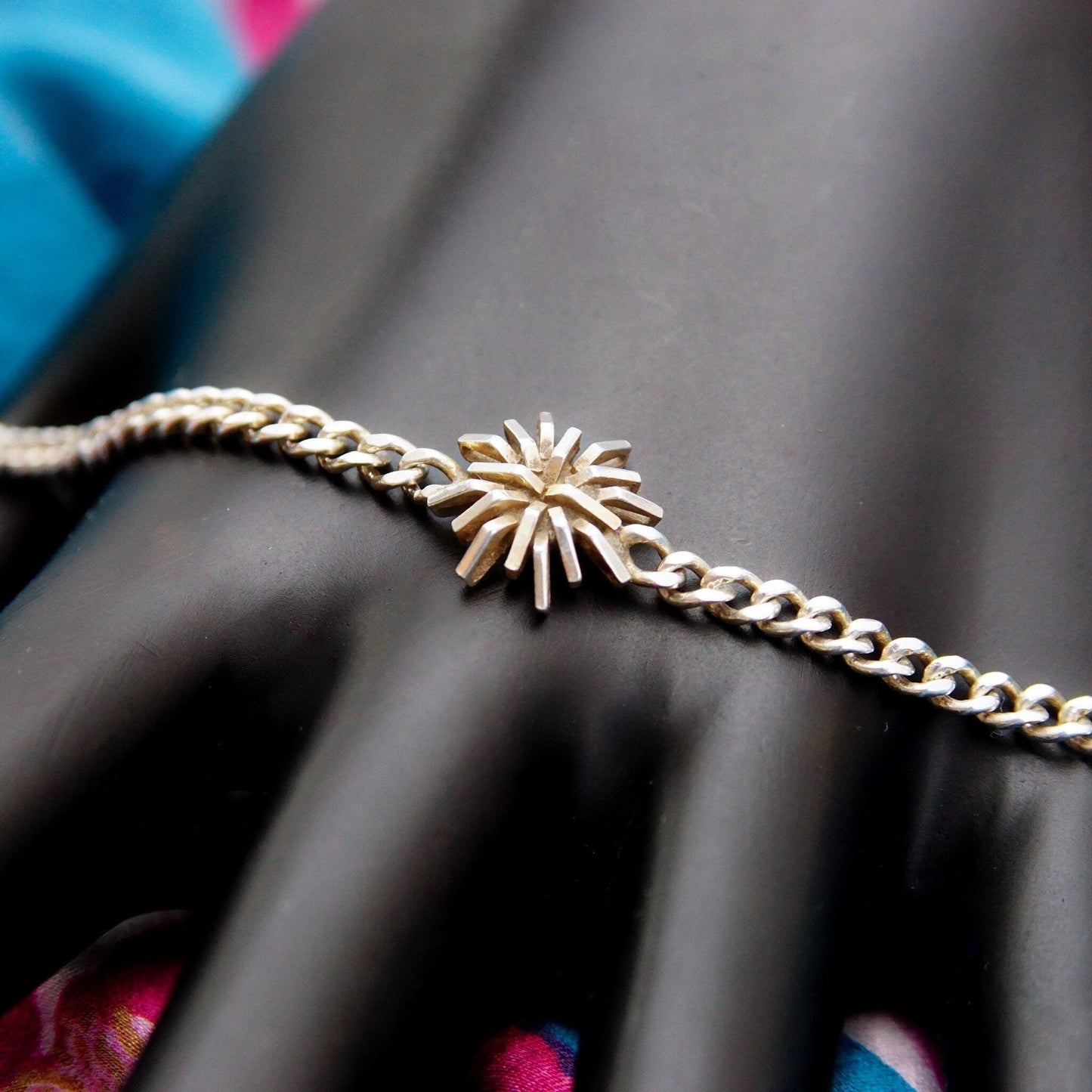 Vintage sterling silver curb link bracelet with starburst flower accent, 3mm curb link chain, unisex, 7 1/2 inches long, on model's hand with colorful background