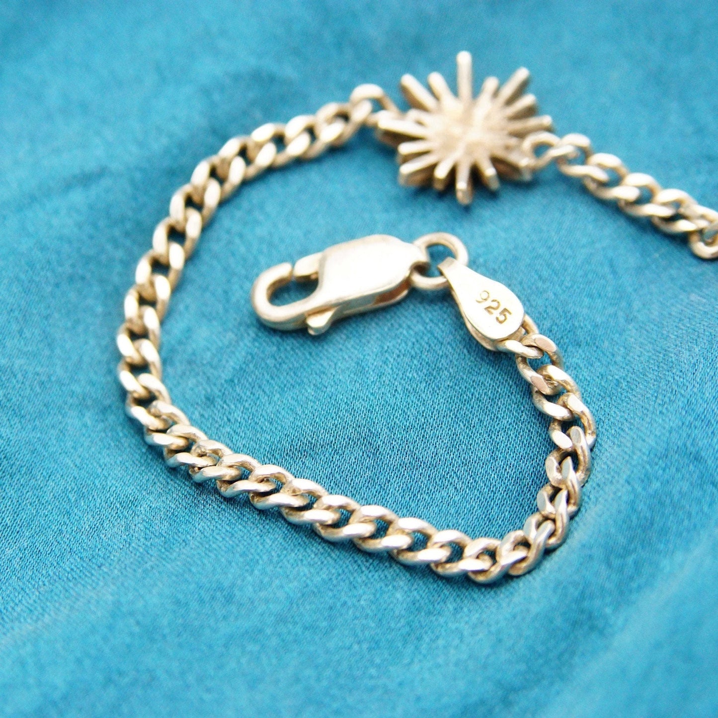 Vintage sterling silver curb link bracelet with starburst flower charm on a blue fabric background, 3mm curb chain, modernist geometric design, unisex style, 7.5 inches long.