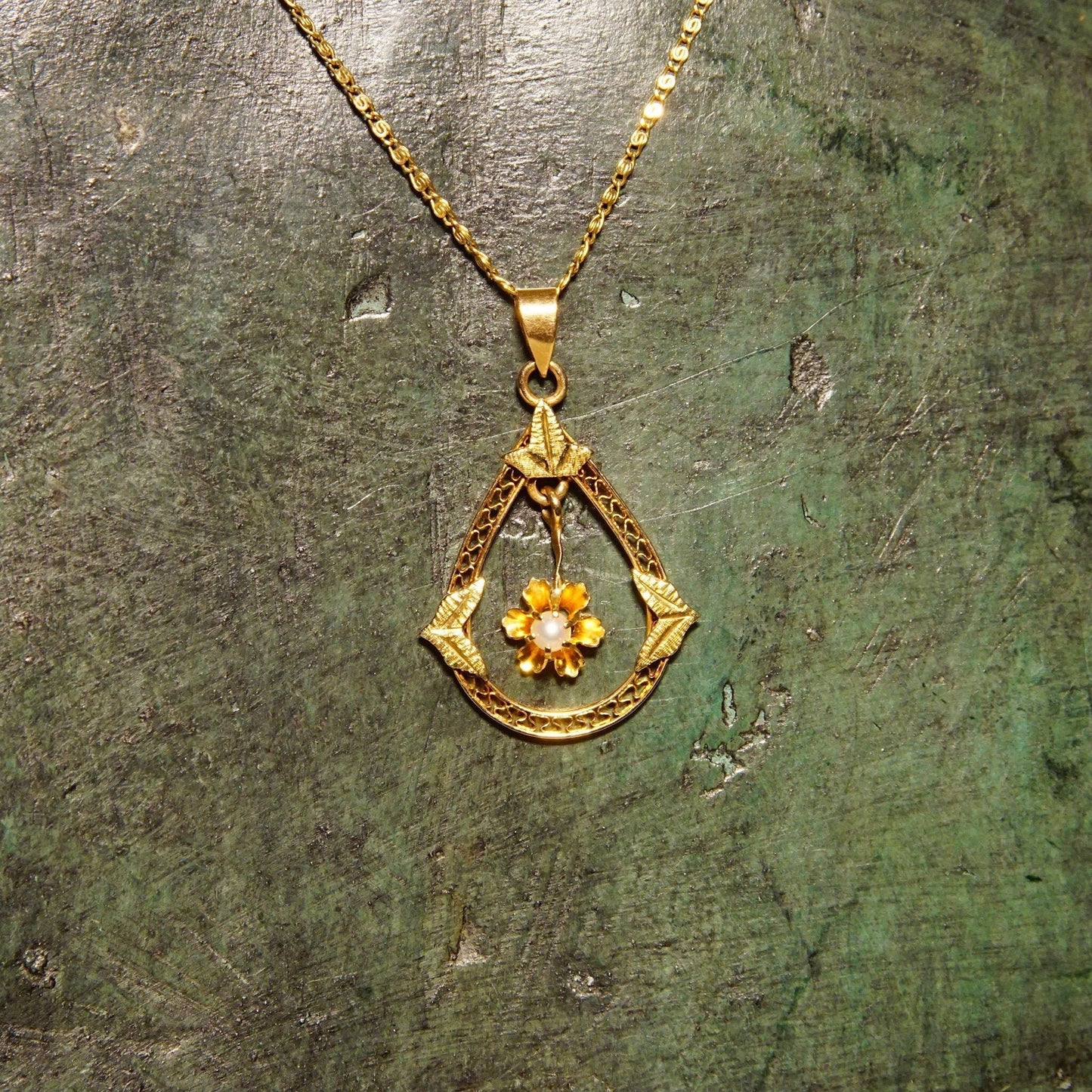 Antique Art Nouveau 14K gold filigree lavalier pendant necklace with seed pearl flower, engraved leaf details, and teardrop shape, measuring 1 1/8 inches long, on textured gold background.