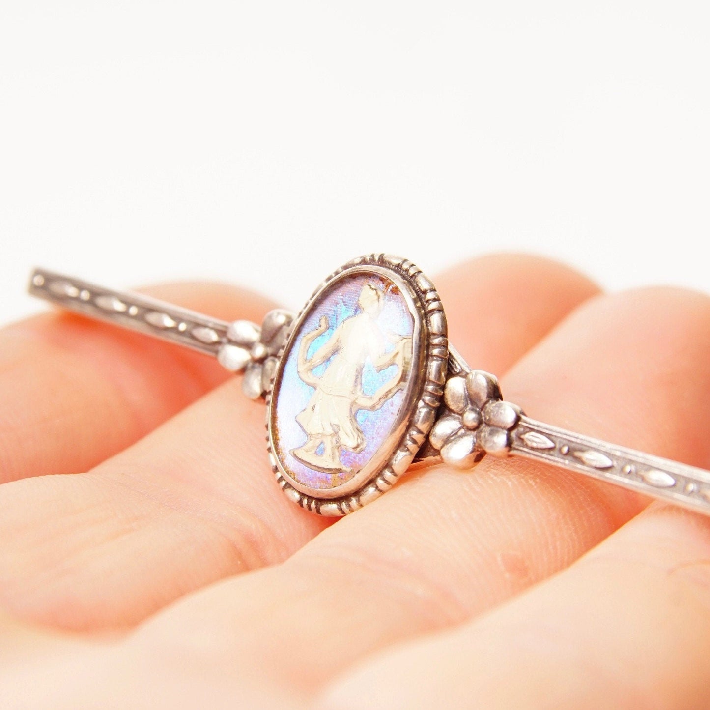 Antique Art Deco sterling silver bar pin with iridescent butterfly wing cameo set in ornate floral frame with engraved accents, measuring 1 3/8 inches long, resting on an open hand to show size and detail.