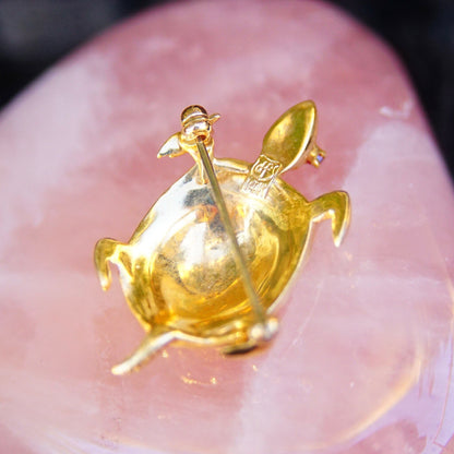 Vintage 14K yellow gold turtle brooch pin with small ruby gemstone eyes, cute animal jewelry piece in close-up on pink background.