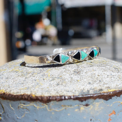 Vintage 70's Zuni inlaid turquoise and onyx silver cuff bracelet with triangle pattern on weathered metal surface