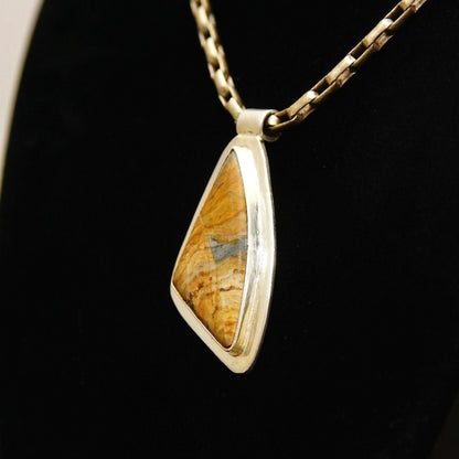 Sterling silver pendant necklace with abstract triangular bezel setting featuring a yellow and brown gemstone or fossil, on a black background