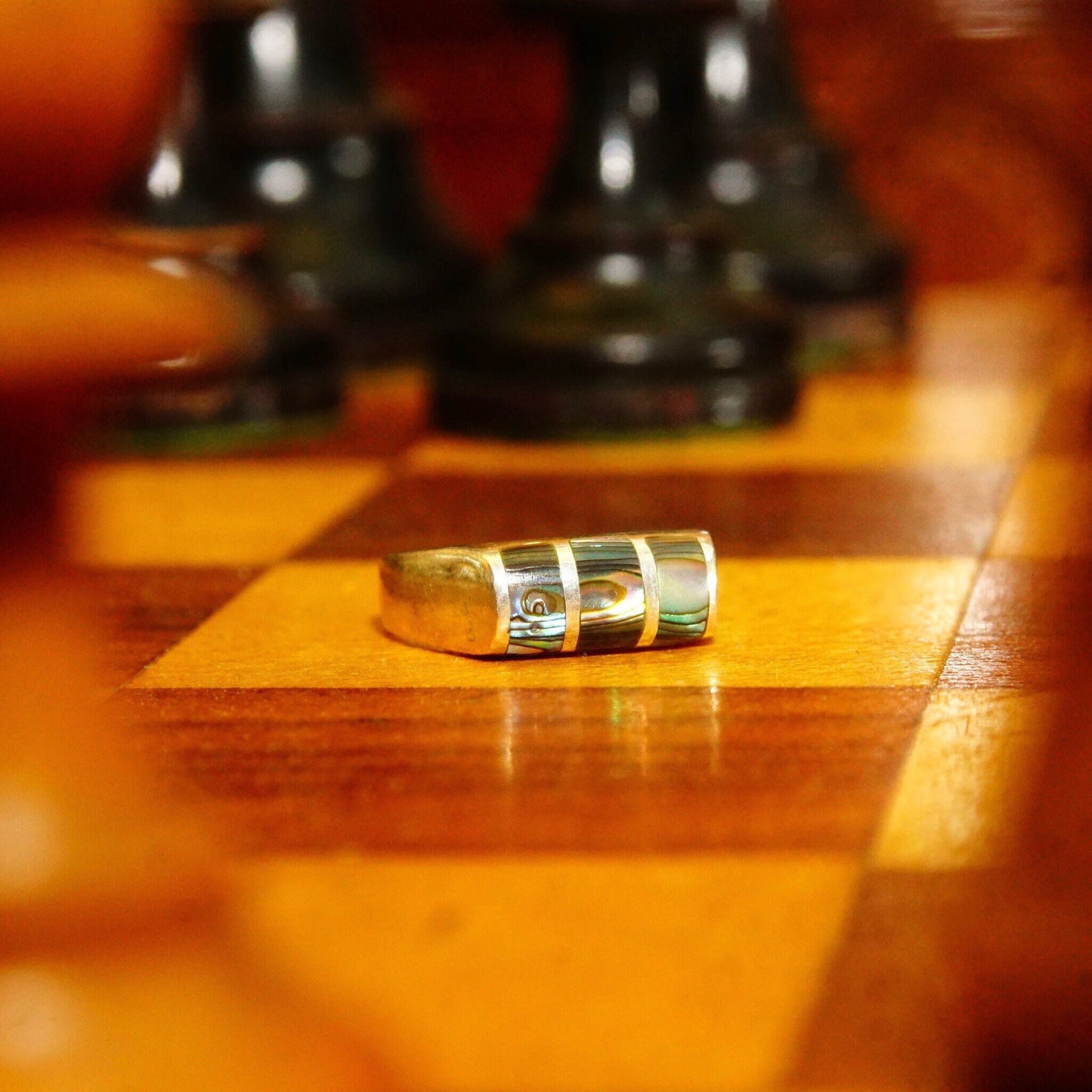 Vintage sterling silver ring with abalone inlay sitting on wooden surface with chess pieces in background