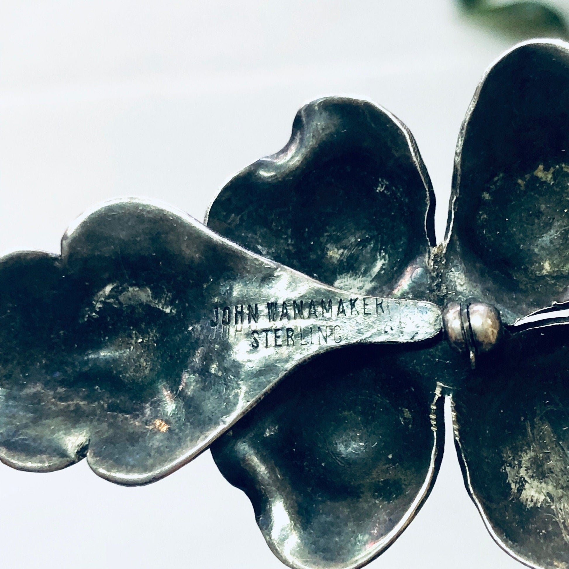 Vintage John Wanamaker sterling silver flower brooch with an aged patina, shaped like a four-leaf clover or shamrock, with the store name engraved on one of the leaves.