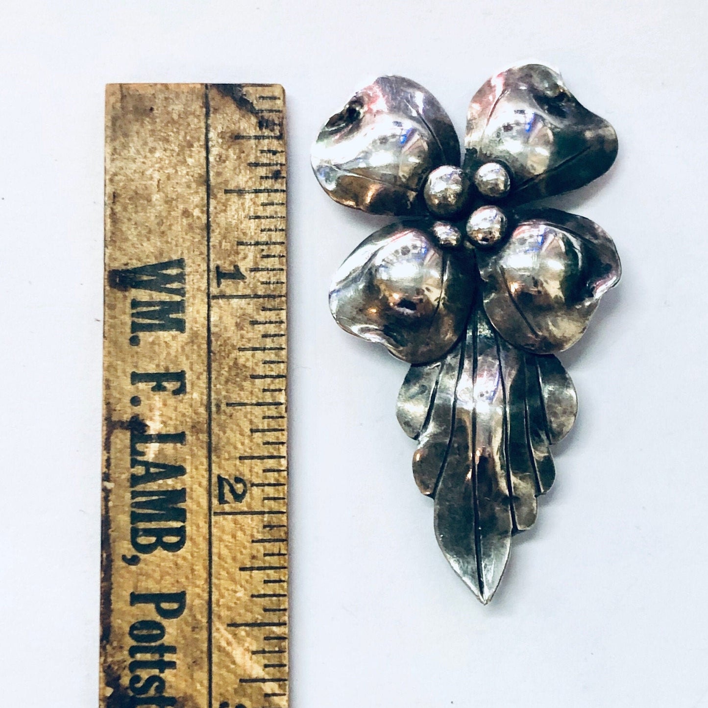 Vintage silver floral brooch pin with four heart-shaped petals from John Wanamaker, shown next to an antique wooden ruler for scale.