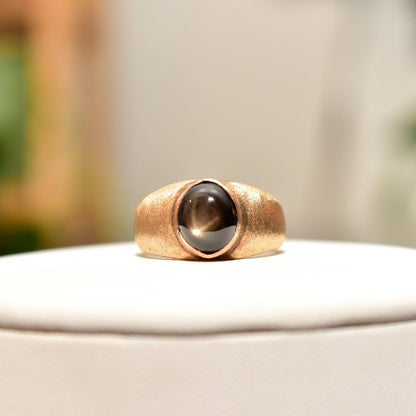14K yellow gold men's pinky ring with black star sapphire gemstone displaying asterism, from estate jewelry collection, ring size 8 3/4 US, shown on white surface with blurred background.