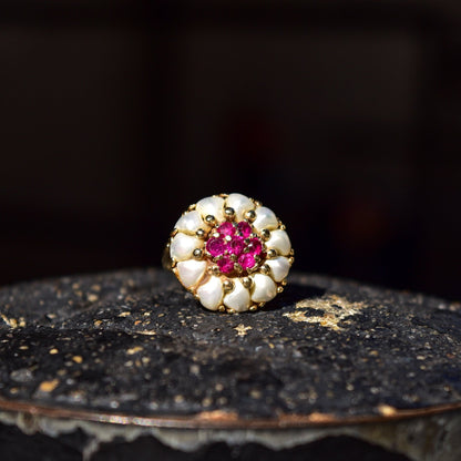 14K yellow gold dome ring featuring a cluster of white pearls surrounding a vivid pink ruby center stone, displayed on a dark textured surface.