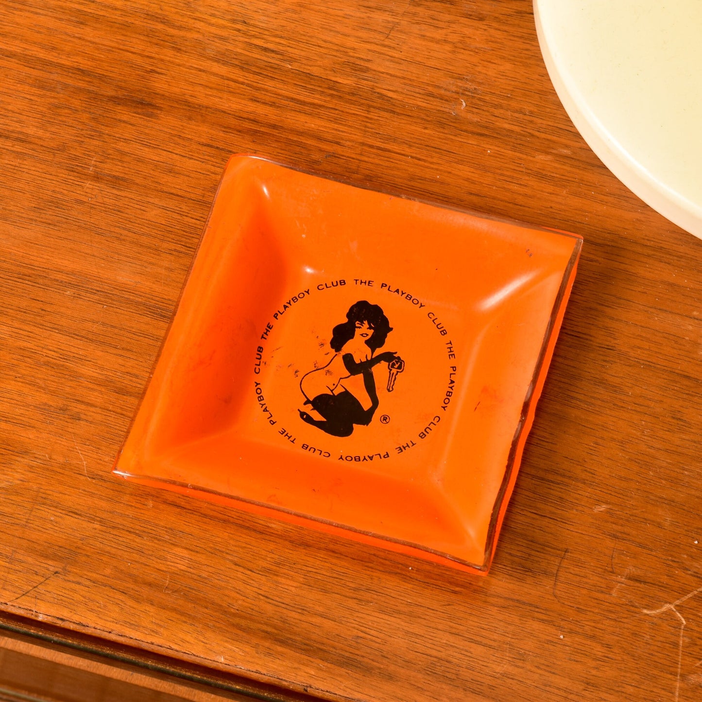 Vintage orange glass ashtray from The Playboy Club in the 1960s featuring a black Leroy Neiman Femlin illustration, measuring 4.75 inches and serving as a small trinket dish.