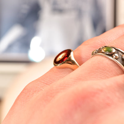 14K yellow gold signet ring with oval cabochon garnet on a hand, with blurred background