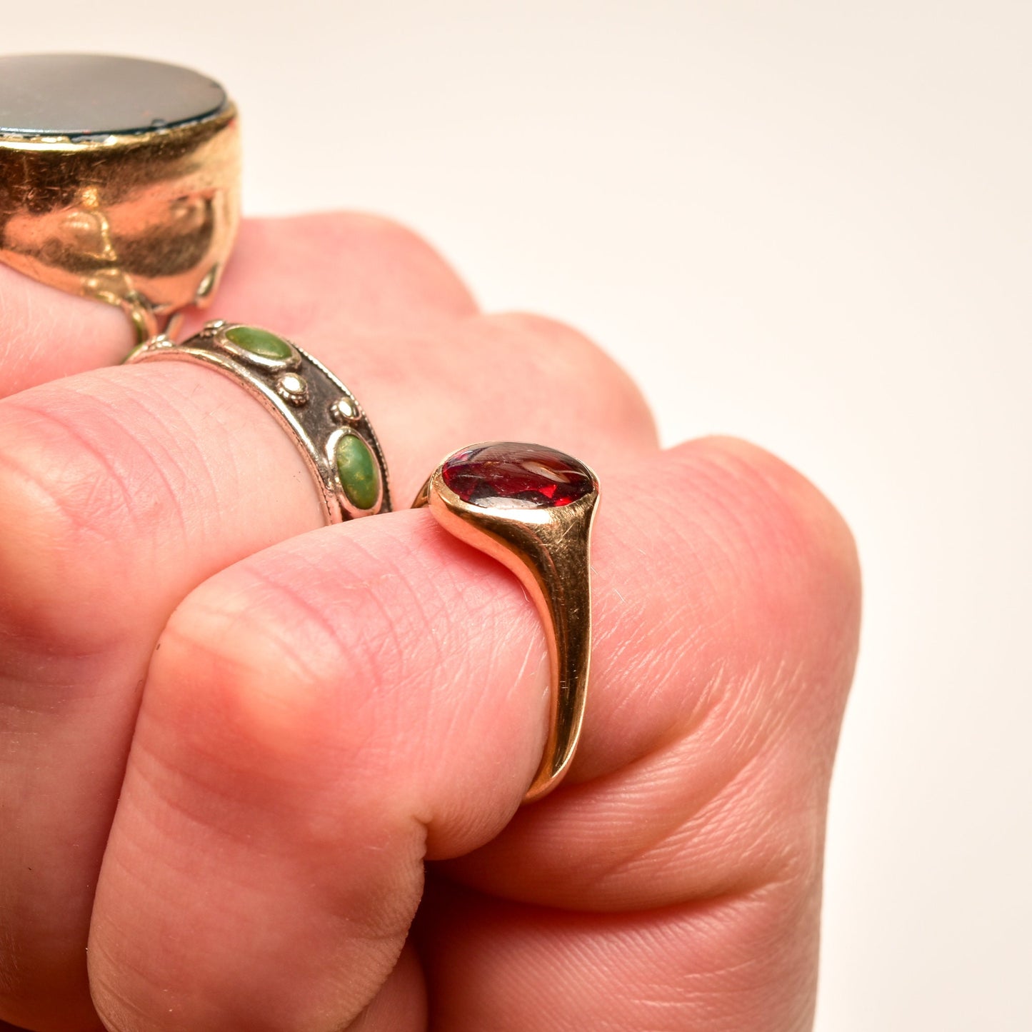 14K yellow gold signet ring with oval cabochon garnet, sleek minimalist design, men's pinky ring size 7, held between fingers against light background