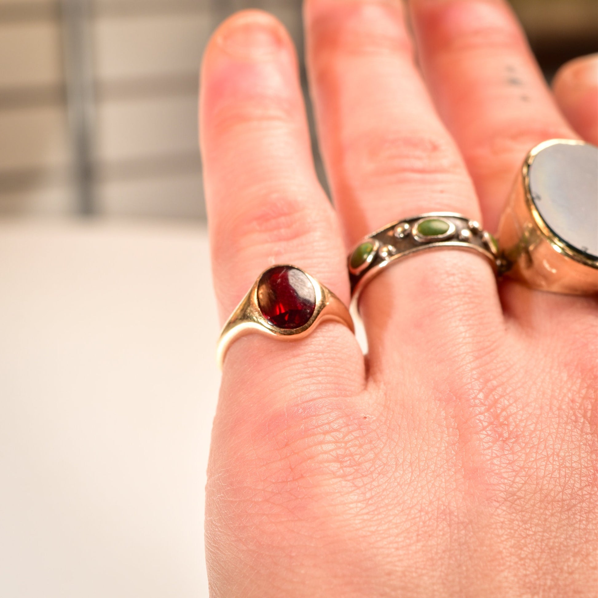 14K yellow gold men's signet ring with cabochon garnet gemstone, showcasing a minimalist design. The ring is worn on a hand, with the garnet stone prominently displayed.