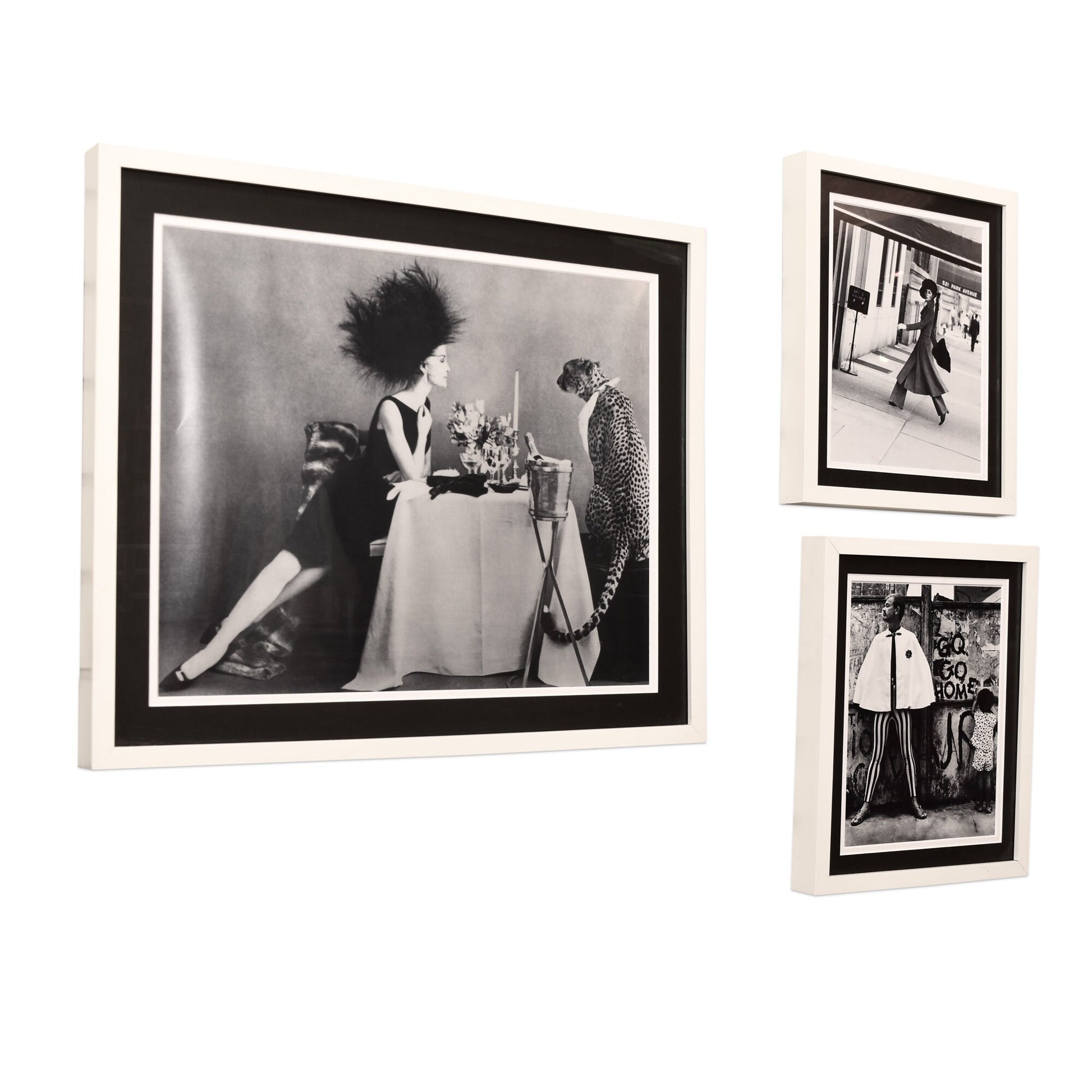 Framed vintage black and white fashion photography prints from Vogue magazine displayed on a white wall, depicting an elegant woman at a dining table and a stylish couple walking together, evoking classic style and glamour.