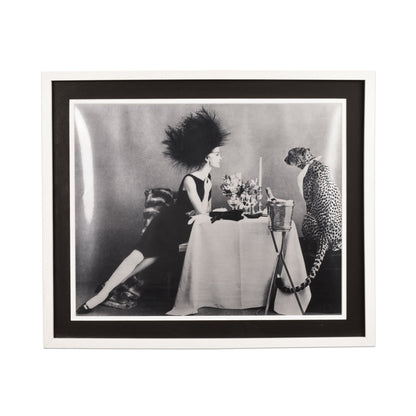 Framed black and white vintage photograph of a glamorous woman at a table arranging flowers, with an exotic cheetah seated beside her, evoking 1960s fashion and style.