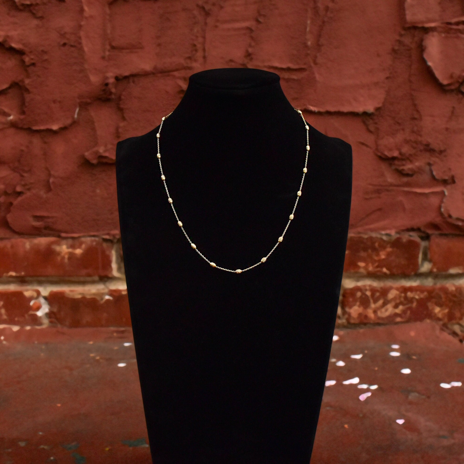 Close-up view of an elegant sterling silver beaded station necklace displayed on a black bust against a rustic red brick wall background.