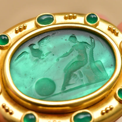18K gold brooch pendant featuring an oval Venetian glass intaglio depicting classical figures, accented with emerald cabochons and a mother of pearl backing.