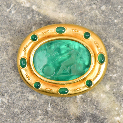 18K gold brooch pendant featuring an oval green Venetian glass intaglio center accented by emerald cabochons, with a mother of pearl backing, by designer Elizabeth Locke. The pendant measures approximately 2 inches wide.