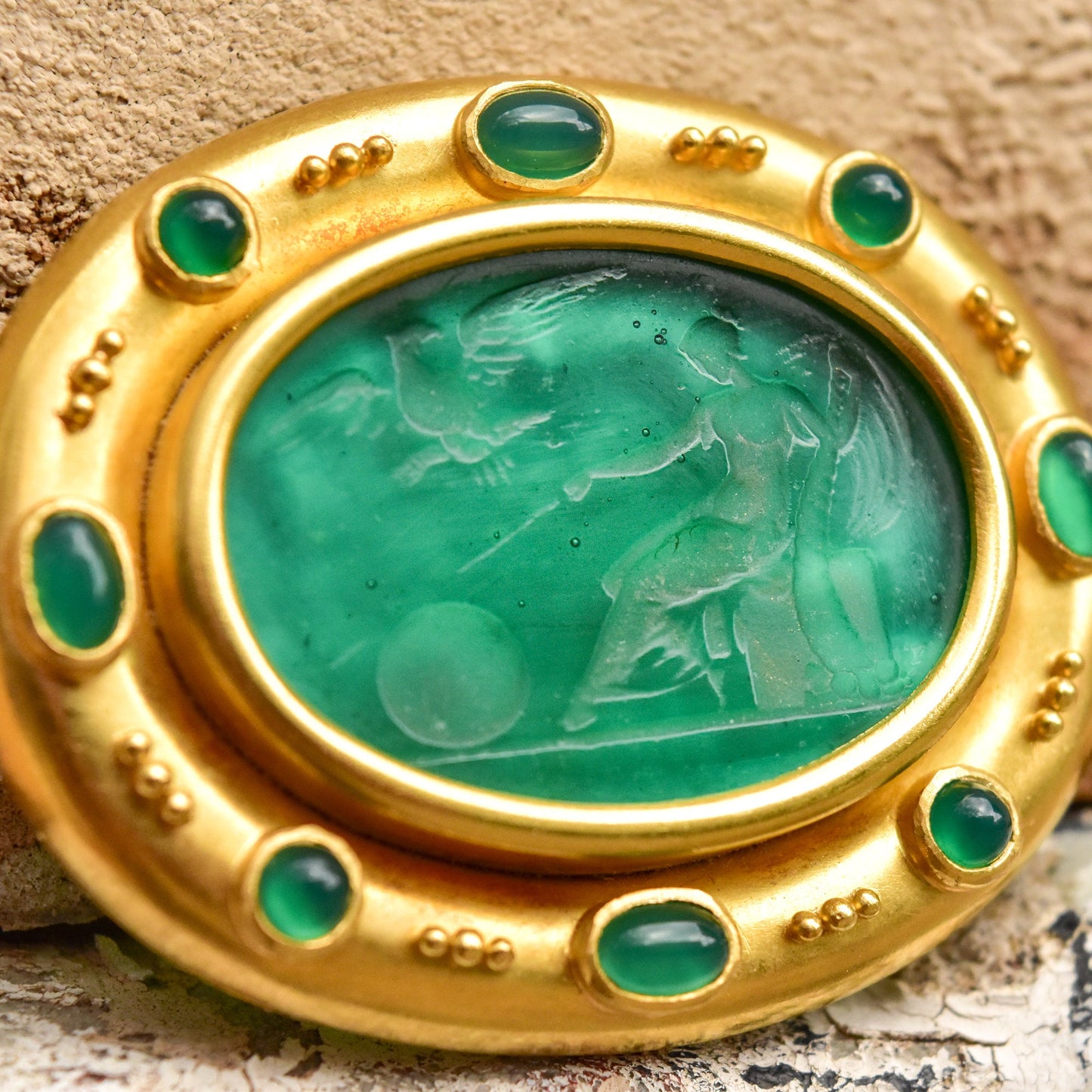 18K gold brooch pendant featuring an oval carved green Venetian glass intaglio center with mother of pearl backing accented by cabochon emeralds, fine jewelry design by Elizabeth Locke.