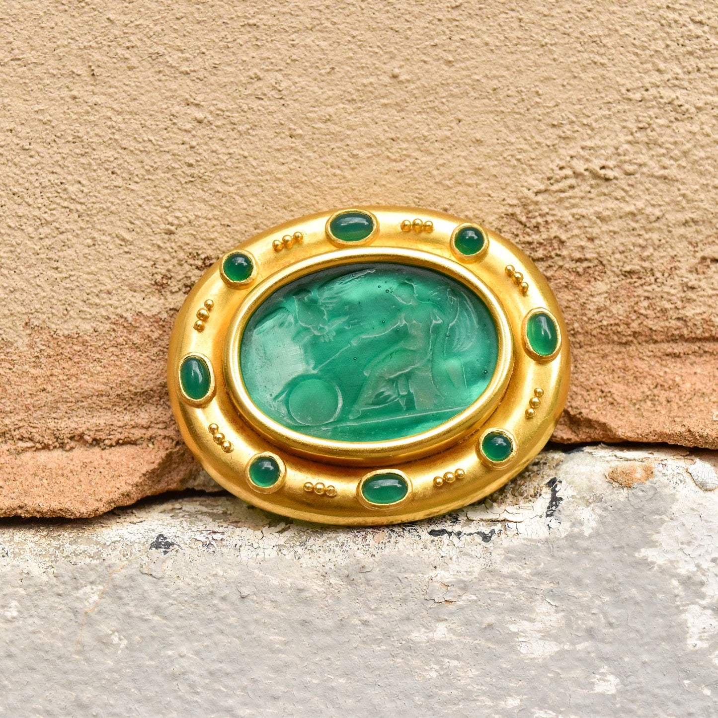 18K gold brooch pendant with oval green venetian glass intaglio center surrounded by emerald cabochons, textured gold rim, mother of pearl backing, 2 inches wide, by designer Elizabeth Locke