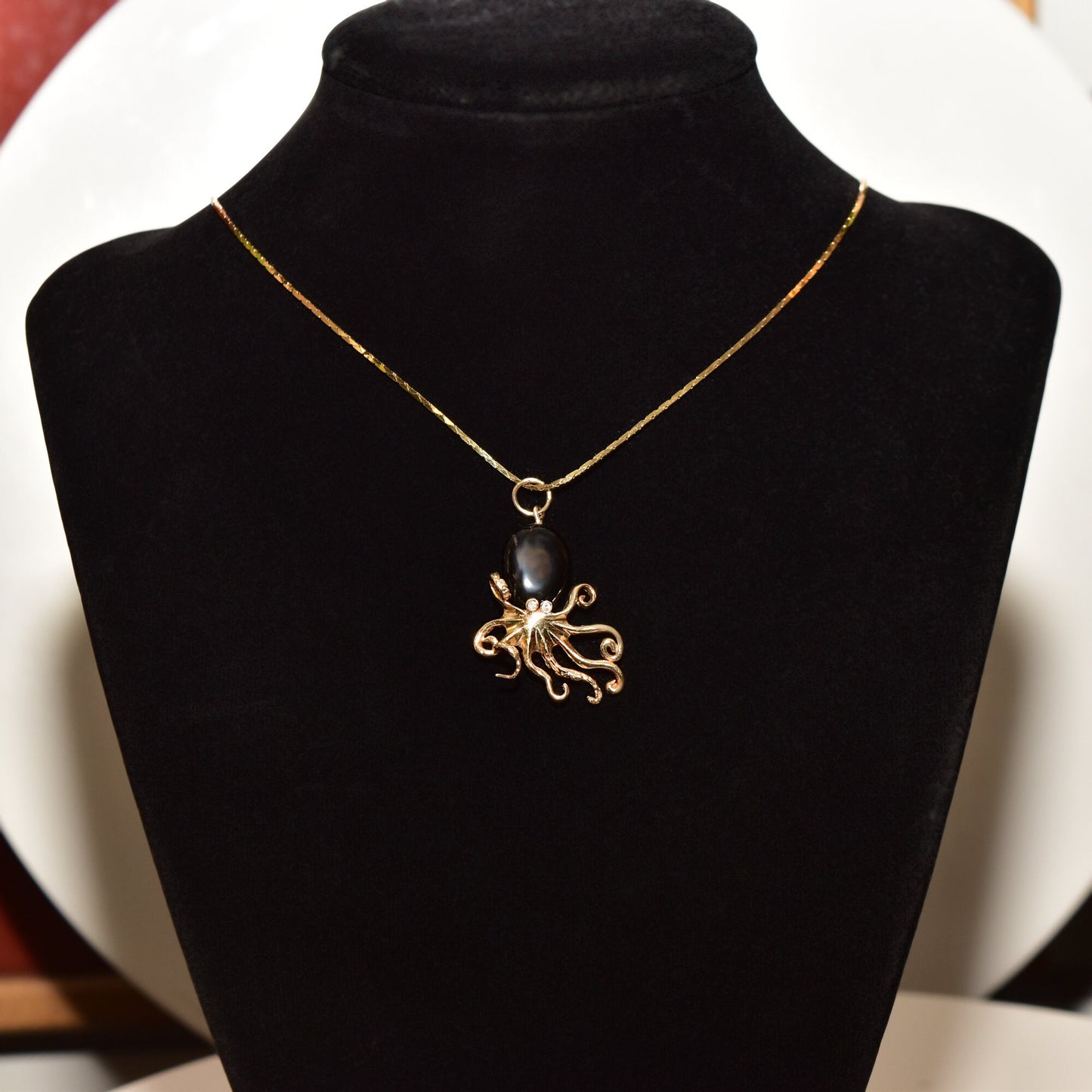 10K yellow gold octopus pendant necklace with black coral body and diamond eye, displayed on black velvet jewelry stand.
