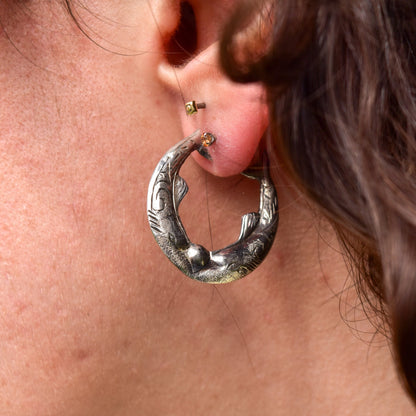 Sterling silver hoop earrings with mirrored etched fish design worn on a woman's ear
