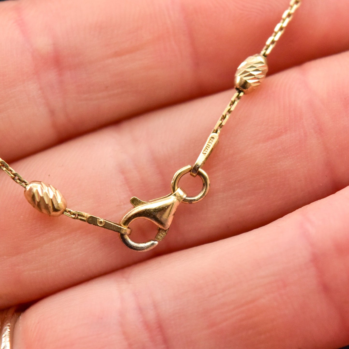 Italian Vermeil sterling silver beaded station necklace with engraved honey dipper beads on a delicate 1mm cable link chain, 17 3/4 inches long, shown in a close-up view held in a person's hand.