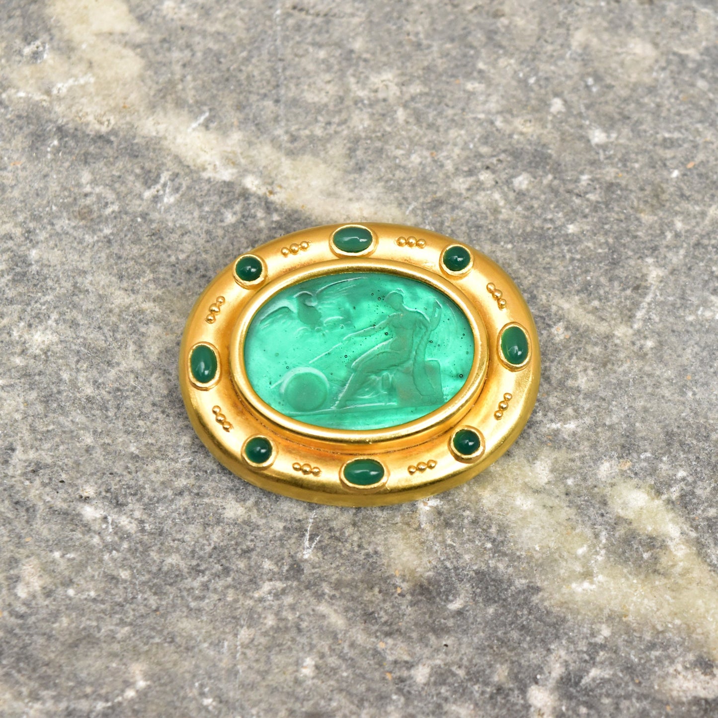 18K gold brooch pendant featuring a green Venetian glass intaglio with emerald cabochons, designed by Elizabeth Locke. The oval intaglio depicts a mythological scene and is set in an ornate gold frame with mother of pearl backing. The brooch measures approximately 2 inches wide.