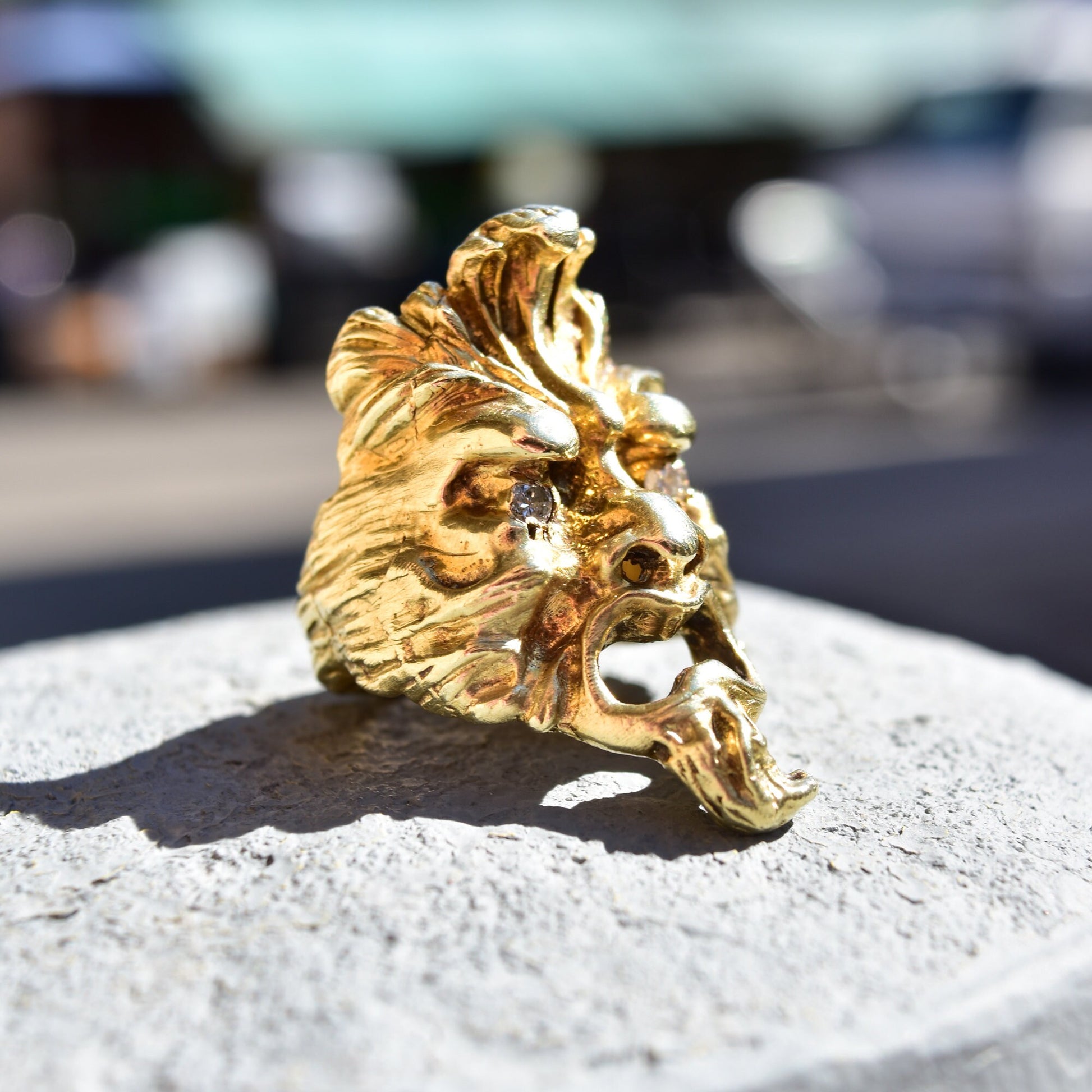 Gold sculpted face ring with diamond eye detail on concrete surface