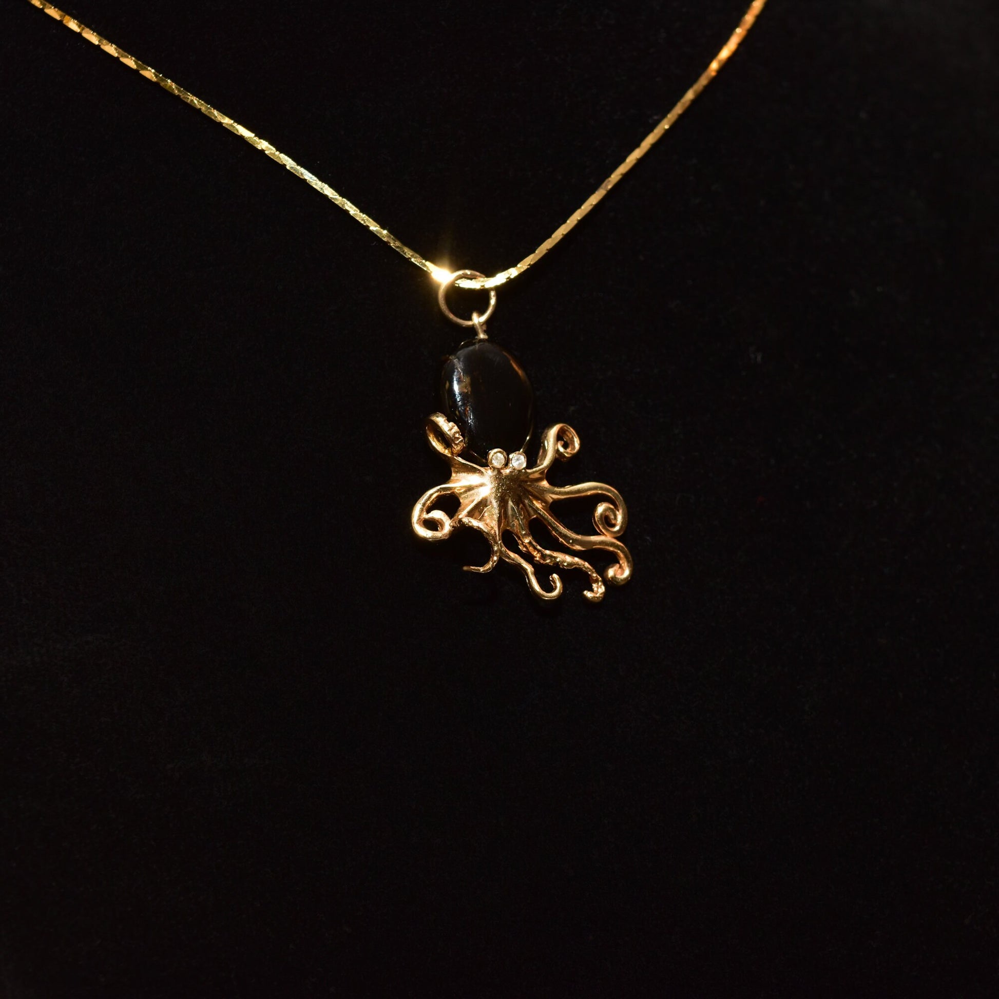 10K yellow gold octopus pendant necklace with black coral and diamond accents on a thin gold chain, showcased against a black background.