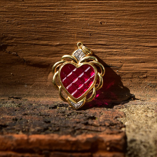 14K yellow gold estate pendant featuring a ruby red glass heart encased in an ornate grid pattern with white gold diamond accents, resting on a rustic wooden surface.
