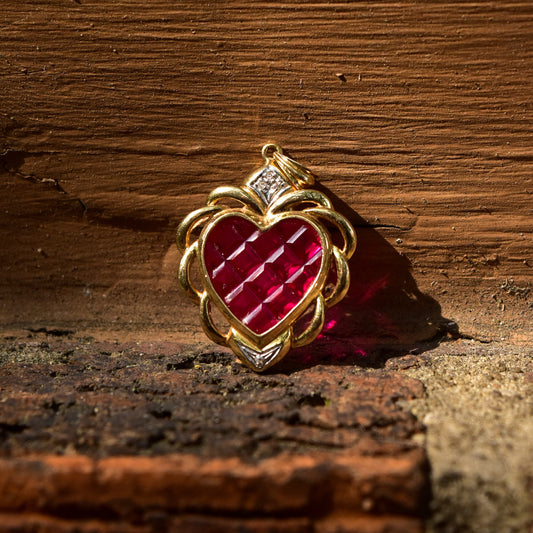 14K yellow gold pendant featuring a 37mm ruby glass heart with white gold diamond accents, an estate jewelry piece resembling the Zelda Heart, resting on a weathered wooden surface with exposed brick background.