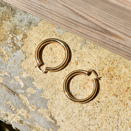 10K yellow gold plated tube hoop earrings, 38mm in diameter, shown on textured stone surface