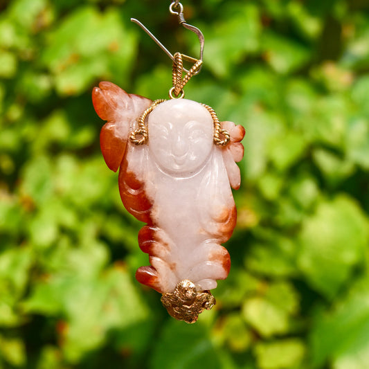 14K yellow gold wire wrapped natural carved red jade Buddha pendant hanging in front of green foliage